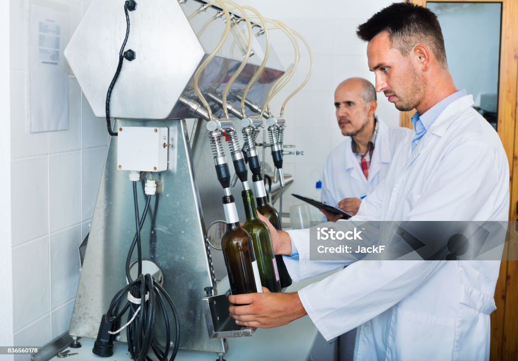 Portrait of male winery worker with bottling machinery on factory Portrait of young smiling male winery worker with bottling machinery on factory Wine Stock Photo