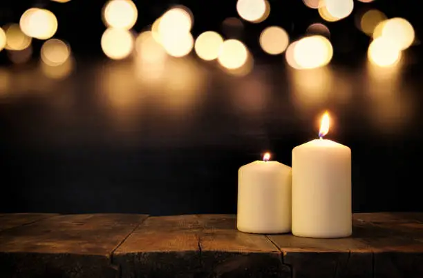 Burning candles over old wooden table with bokeh lights.