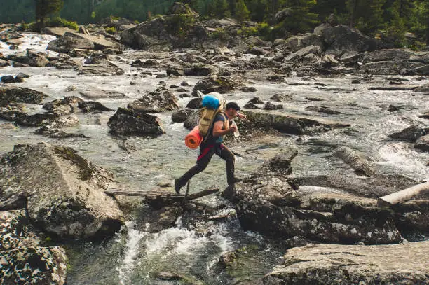 Young Hiker crossing mountain river. Fany mountain. Hiking river crossing on the stones. Tadjikistan