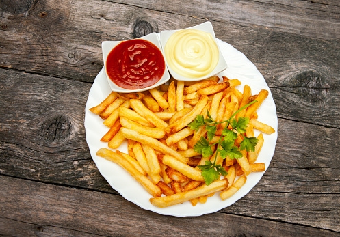 Top view on plate with french fries, tomato sauce and mayonnaise in small bowls on wooden table