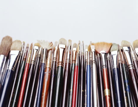 Horizontal straight line of assorted artist's paintbrushes of different sizes and types lined up against a bright clean marble background with one standing out from the others in the middle.