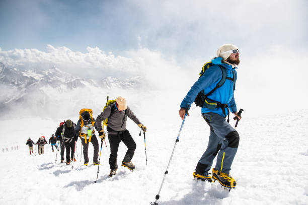 A group of mountaineers climbs to the top of a snow-capped mountain stock photo