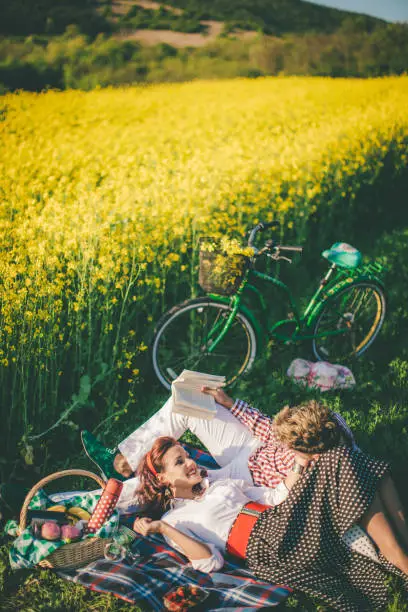 Photo of Happy couple laughing while reading book at picnic