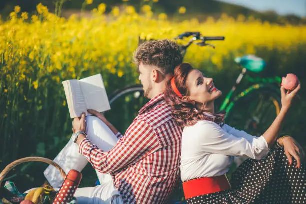 Photo of Happy couple laughing while reading book at picnic