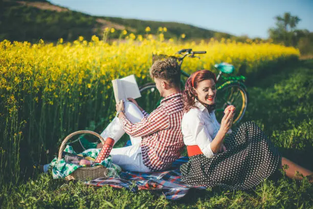 Happy couple laughing while reading book at picnic