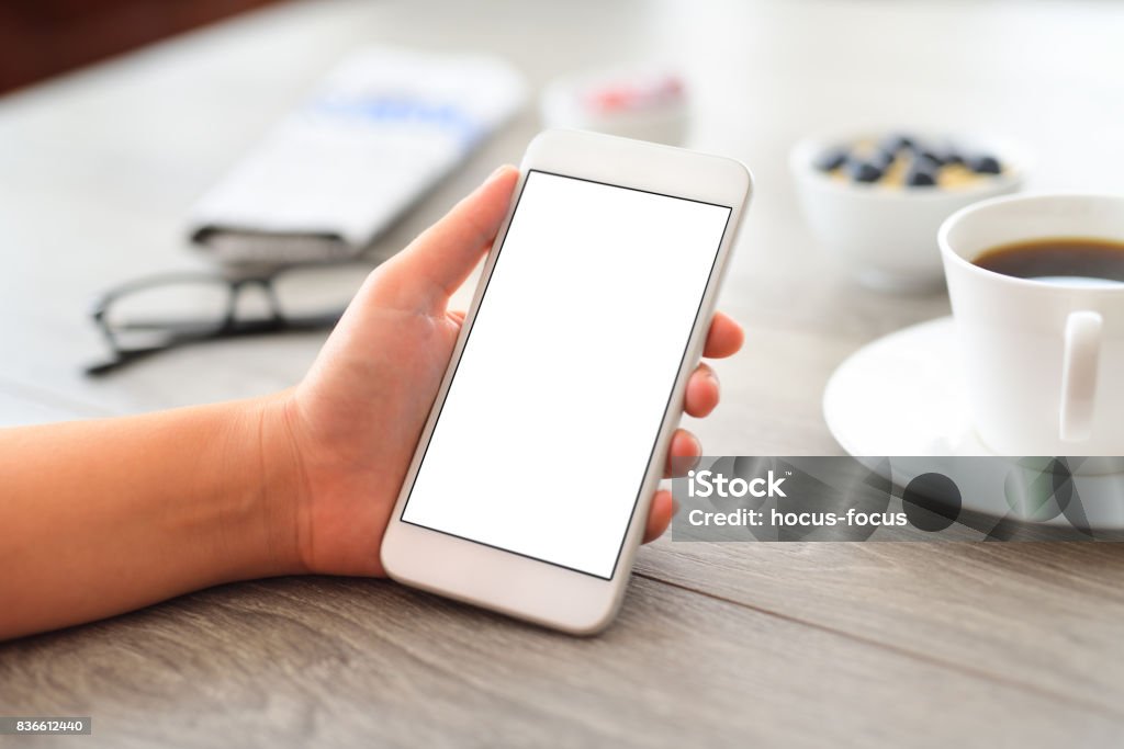 Using white screen smart phone Woman using blank white screen smart phone on a wooden desk. Mobile Phone Stock Photo