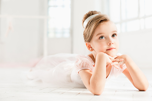 The little balerina in white tutu in class at the ballet school lying on the wooden floor