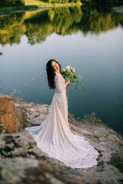 istock Young bride standing on rocky river bank, sunset 836637324