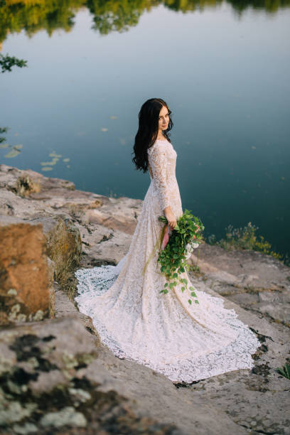 istock Young bride standing on rocky river bank, sunset 836637470