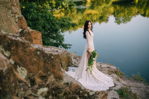 istock Young bride standing on rocky river bank, sunset 836637584