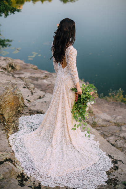 istock Young bride standing on rocky river bank, sunset 836638148