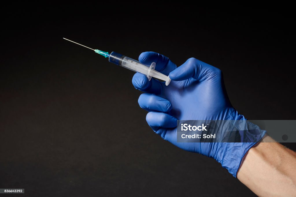 Hand with syringe A hand with a blue operating glove on a needle / syringe Syringe Stock Photo