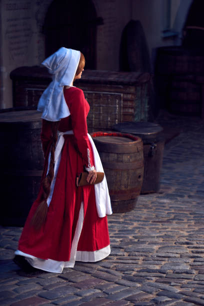Townswoman in red dress with an apron and chaperone on the street. Costume stylized of later Middle Ages on 15/ 16th century. stock photo