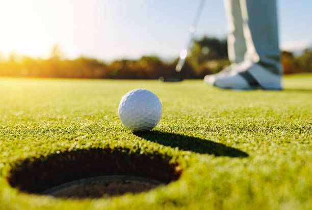 Professional golfer putting ball Professional golfer putting ball into the hole. Golf ball by the edge of hole with player in background on a sunny day. golf stock pictures, royalty-free photos & images