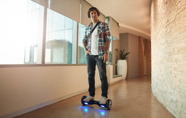 Young man on an electrical self-balancing scooter in office Full length shot of stylish young man riding on electrical self-balancing scooter in modern office corridor. hoverboard stock pictures, royalty-free photos & images