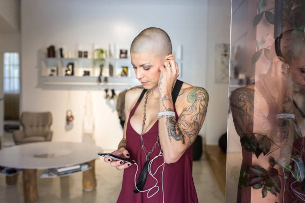 женщина с бритой головой проверяет смартфон - headphones women tattoo music стоковые фото и изображения