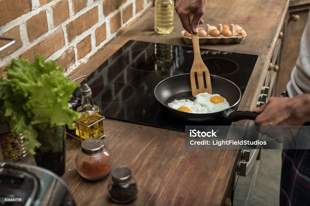 partial view of young man preparing eggs for breakfast in kitchen at home Glass-Ceramic Stove Top Stock Photo