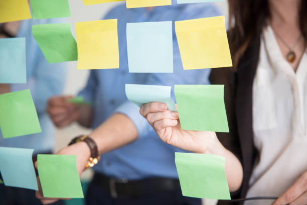 midsection of business people sticking adhesive notes on glass - transparent holding glass focus on foreground imagens e fotografias de stock