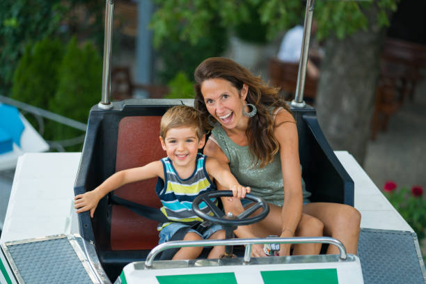 cheerful smiling mother and three year old son enjoying ride with toy car in funpark in summer