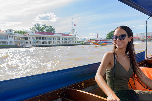 Portrait of young beautiful multi-ethnic tourist woman riding thai taxi boat while exploring the city of Bangkok Thailand horizontal shot