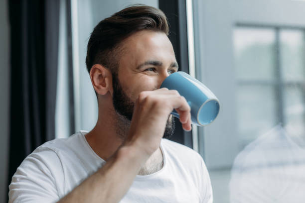 istock handsome young man drinking tea from cup and looking at window at home 836665546