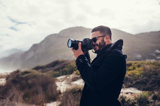 Handsome man with digital camera outdoors. Young male photographer photographing in nature on winter day.