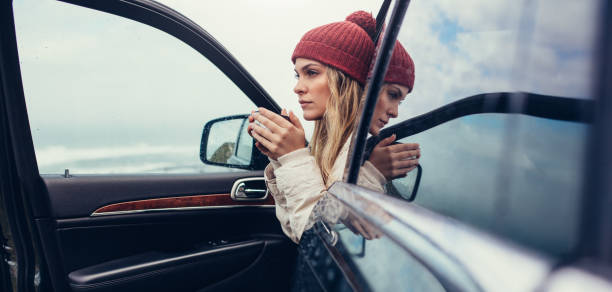 Beautiful young female with coffee in hand sitting in a car. Female on road trip drinking coffee inside car.