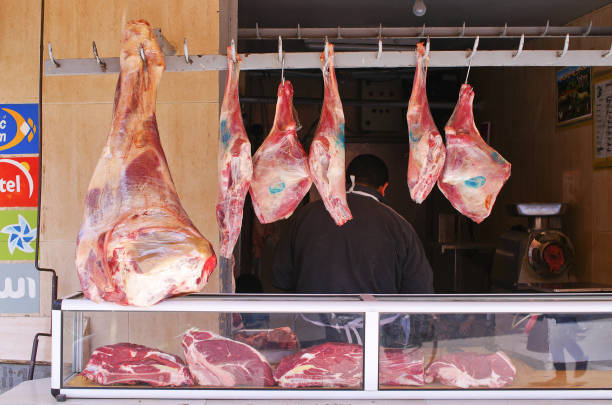 Pieces of fresh beef meet hanging on metal hooks in butchery refrigerator room, viewed from low angle