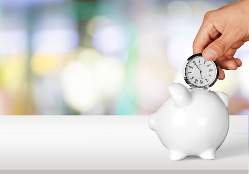 Hand depositing  clock  in piggy bank on background