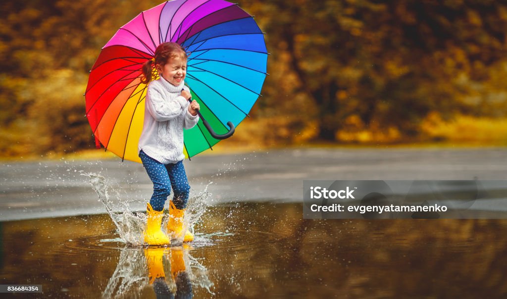 Felice ragazza divertente bambino con ombrello saltando su pozzanghere in stivali di gomma - Foto stock royalty-free di Bambino