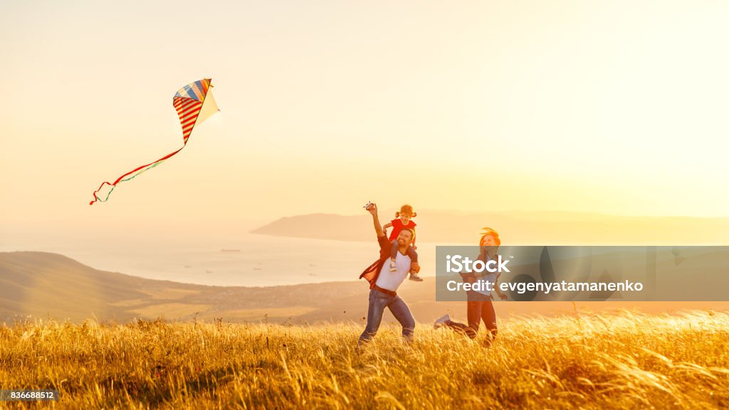 Feliz familia padre hija madre e hijo lanzar una cometa en naturaleza al atardecer - Foto de stock de Familia libre de derechos