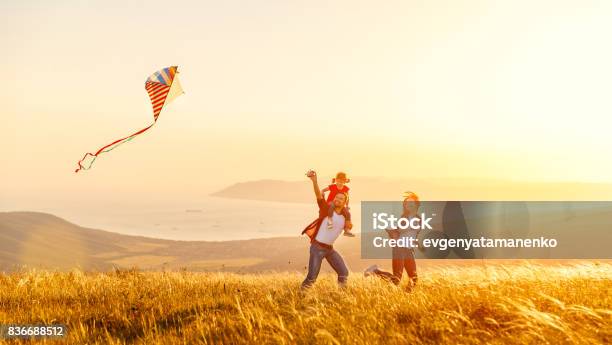 Feliz Familia Padre Hija Madre E Hijo Lanzar Una Cometa En Naturaleza Al Atardecer Foto de stock y más banco de imágenes de Familia