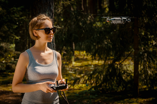 Young woman holding radio controller and flying a drone in a forest