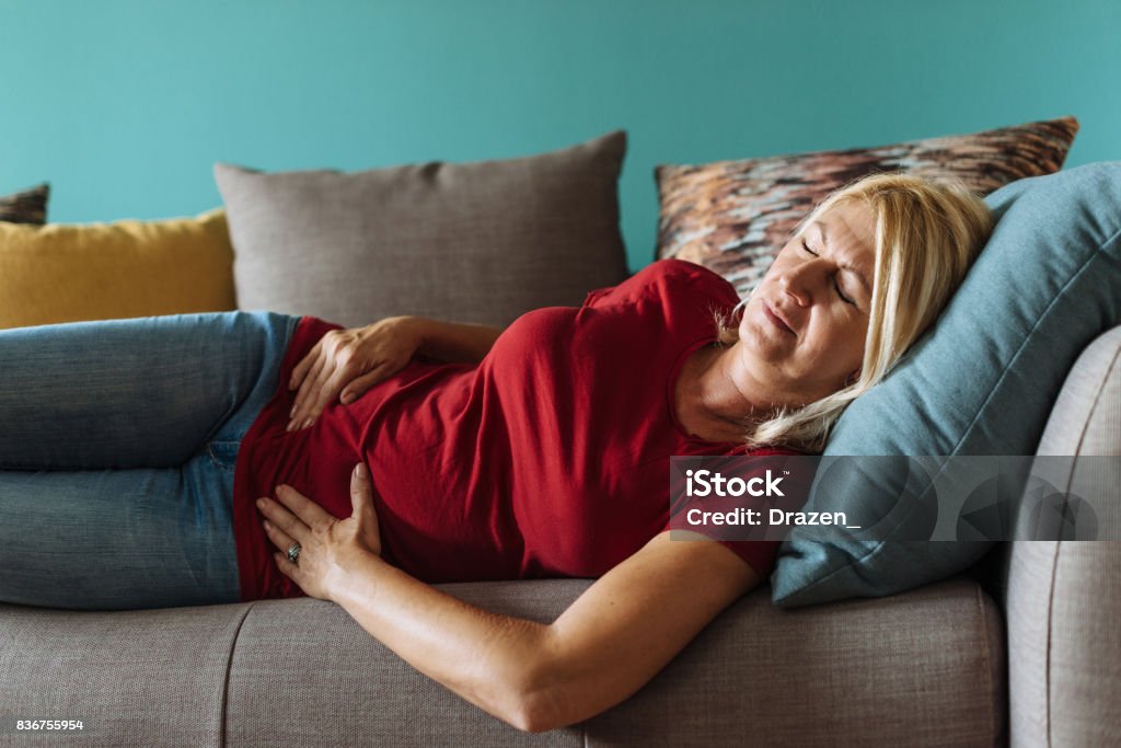 Femme mature face à des douleurs pelviennes à la maison - Photo de Maux d'estomac libre de droits