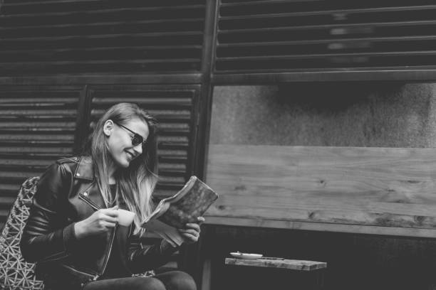 Black and white photo of a Young beautiful woman sitting in cafe shop, drinking coffee and reading newspaper