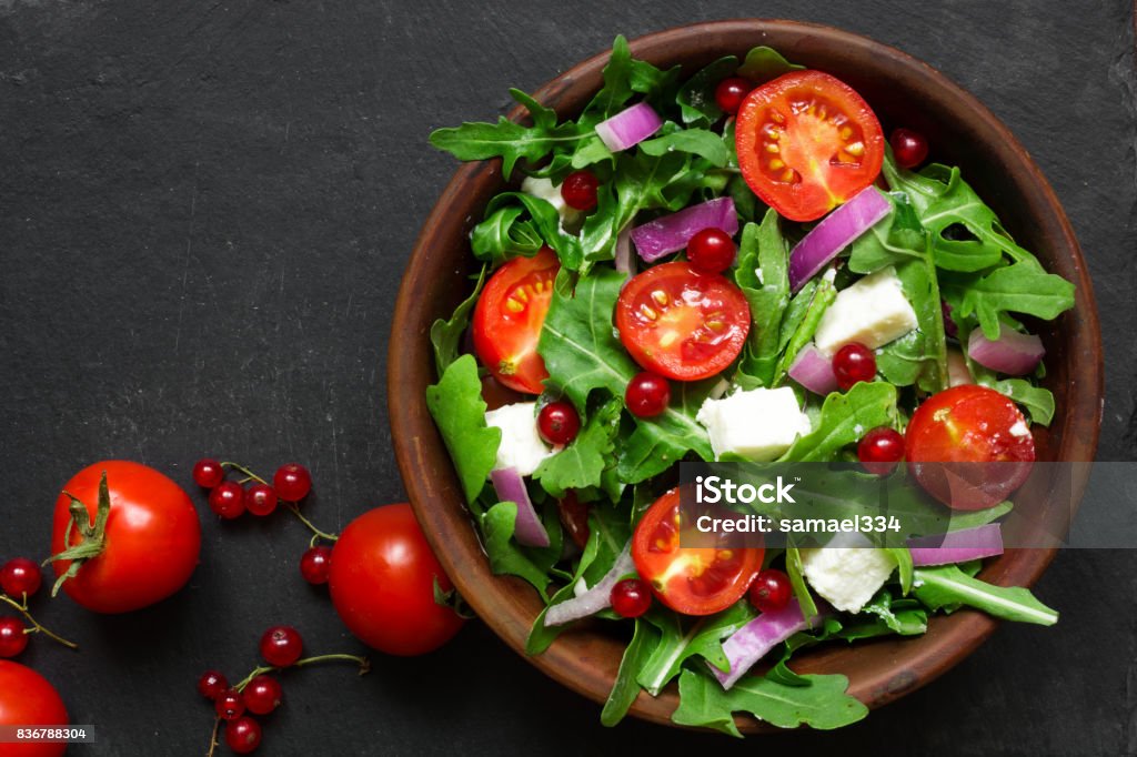 Salade de roquette, fromage feta, oignon rouge et aux groseilles rouges dans un bol - Photo de Salade composée libre de droits