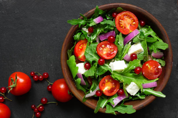 Fresh salad with arugula, feta cheese, red onion and red currant in a bowl Fresh salad with arugula, feta cheese, red onion and red currant in a bowl on chalkboard background with copy space. top view spring mix lettuce leaves stock pictures, royalty-free photos & images