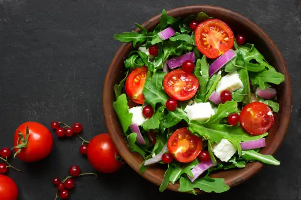 Photo of Fresh salad with arugula, feta cheese, red onion and red currant in a bowl