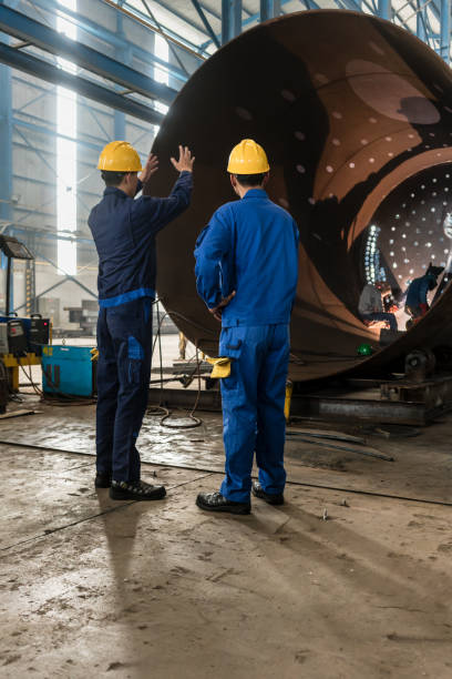 Workers supervising the manufacture of a metallic cylinder Two experienced workers supervising the manufacture of a metallic cylinder in the interior of a factory boiler photos stock pictures, royalty-free photos & images