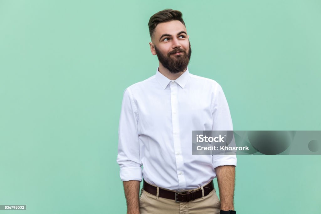 Flying of thoughts. Thoughtful bearded businessman looking away while standing against light green wall. Studio shot Colored Background Stock Photo