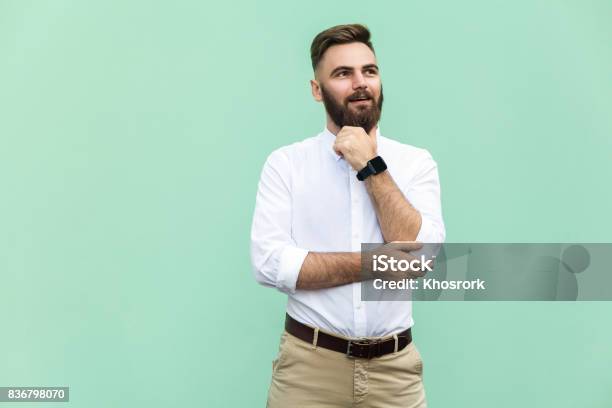 Thoughtful Bearded Businessman Looking Away While Standing Against Light Green Wall Studio Shot Stock Photo - Download Image Now
