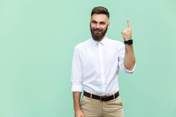 junge erwachsene geschäftsmann hat eine idee, mit finger zeigen bis auf leichte grüne wand hintergrund isoliert. aufgeregt kerl mit lösung für ein problem. menschliches gesicht ausdruck körpersprache, wahrnehmung kreativität leben. studio gedreht - surprise ideas business person pointing stock-fotos und bilder