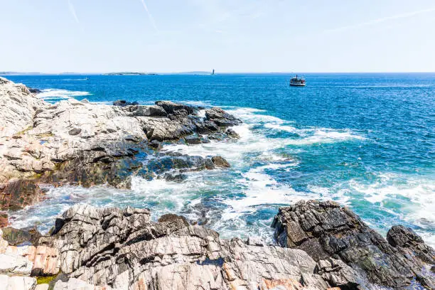 Cliff rocks by trail by Portland Head Lighthouse in Fort Williams park in Cape, Elizabeth Maine during summer day with ferry boat