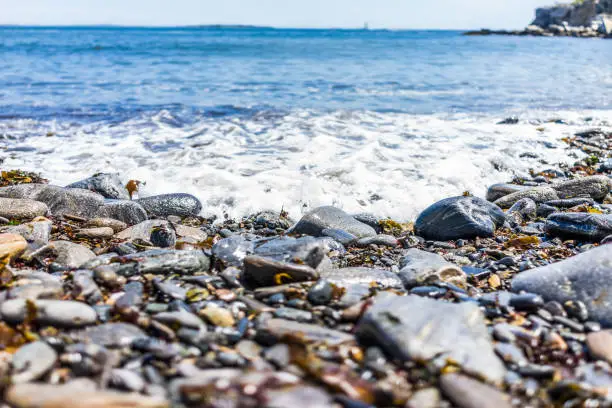 Rocky public beach called Ship Cove by Portland Head Lighthouse in Cape Elizabeth, Maine with closeup of water and stones on ground level
