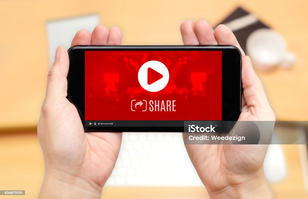 Watching two hand holding mobile phone with play and share icon on screen and blur desk office background,Digital content concept Watching two hand holding mobile phone with play and share icon on screen and blur desk office background,Digital content concept. Internet Stock Photo