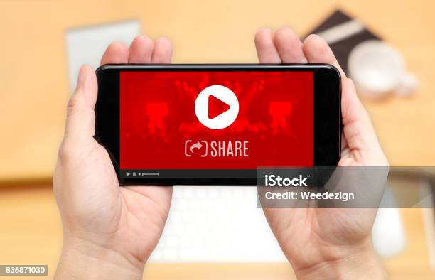 Watching Two Hand Holding Mobile Phone With Play And Share Icon On Screen And Blur Desk Office Backgrounddigital Content Concept Stock Photo - Download Image Now