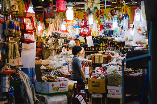 Chinatown, Singapore - December 27, 2015: One woman in a market stall full of non-perishable foods on the wet market in Chinatown, Singapore.