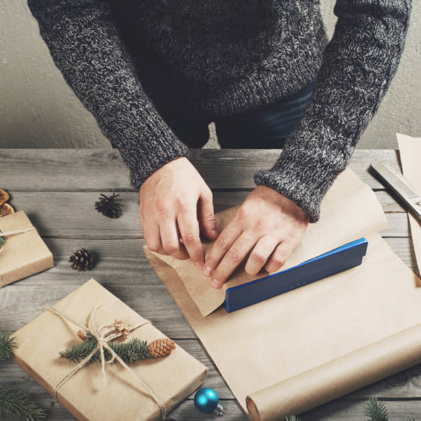 Male hands wrap Christmas gift on wooden table