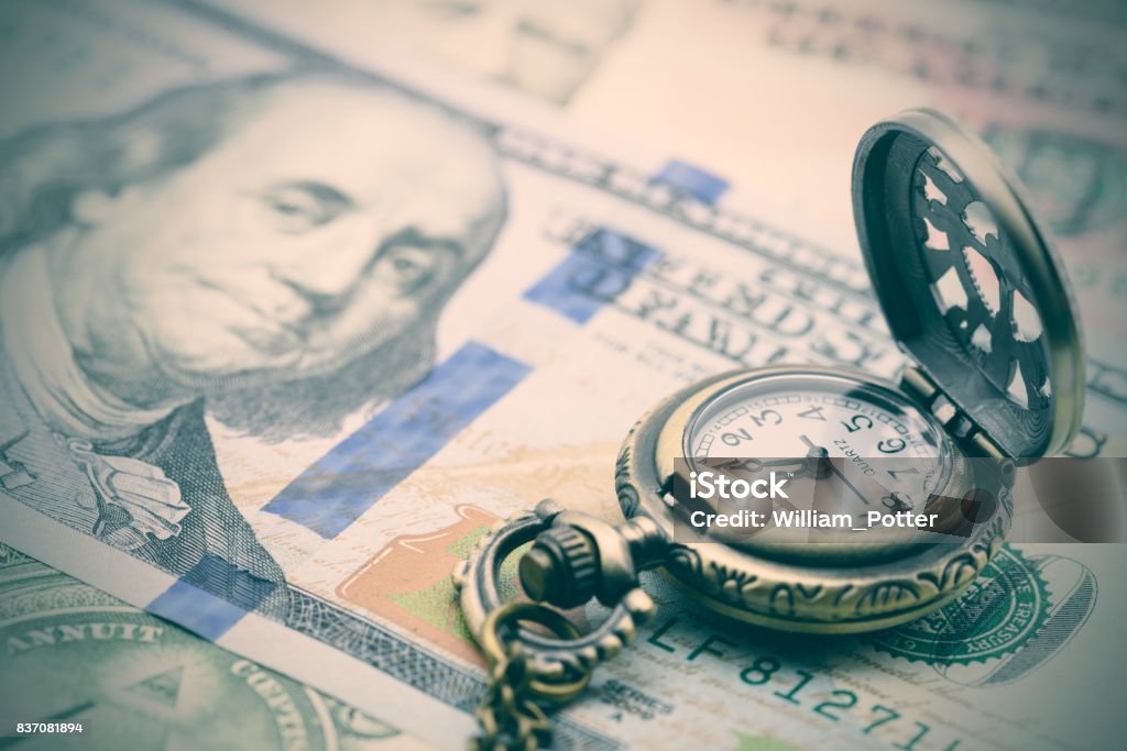 Classic pocket watch on a hundred US dollar bill. Vintage / retro color style : Classic pocket watch on a hundred US dollar bill. A concept / idea of time value of money (TVM), money in hand today is worth more than the same amount in the future. Clock Stock Photo