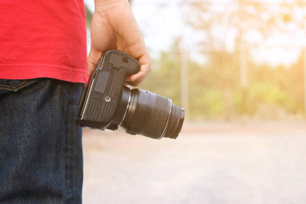 istock Back view of young photographer holding camera on hands with sunshine effect background. 837089152